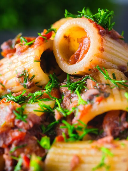 Close-up sardine and tomato pasta Bolognese or ragu garnished with fresh basil.