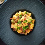 Overhead sardine and tomato pasta Bolognese or ragu garnished with fresh basil.