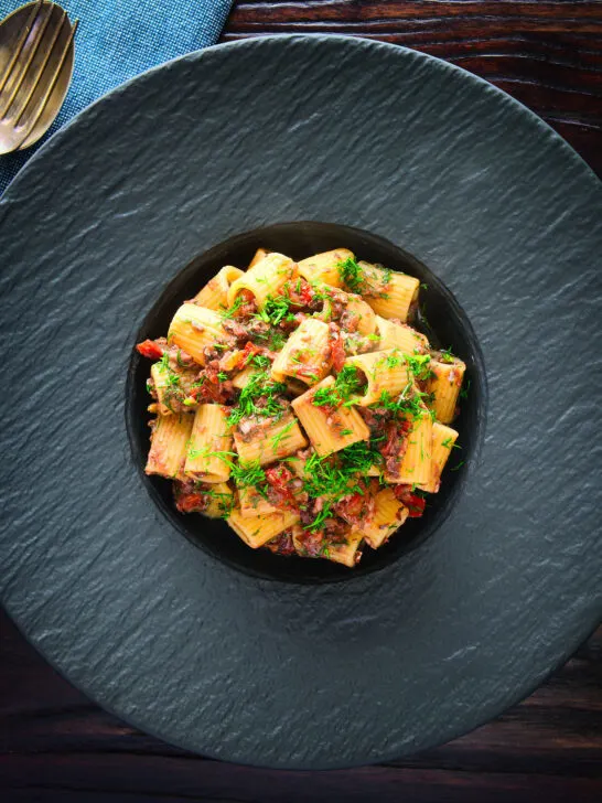 Overhead sardine and tomato pasta Bolognese or ragu garnished with fresh basil.