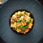 Overhead sardine and tomato pasta Bolognese or ragu garnished with fresh basil.