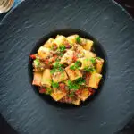 Overhead sardine and tomato pasta Bolognese or ragu garnished with fresh basil.