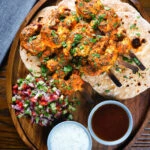 Overhead Indian tandoori king prawns skewers with chapatis, kachumber salad and dipping sauces.