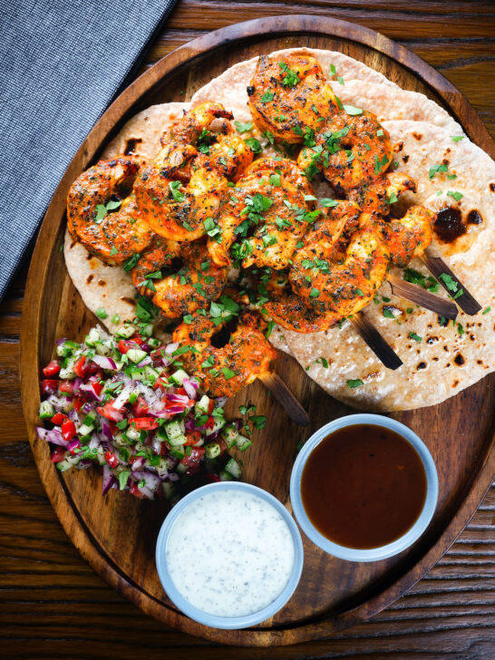Overhead Indian tandoori king prawns skewers with chapatis, kachumber salad and dipping sauces.