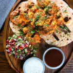 Overhead Indian tandoori king prawns skewers with chapatis, kachumber salad and dipping sauces.