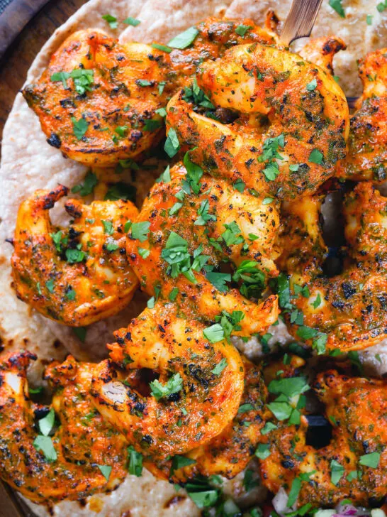 Overhead close-up Indian tandoori king prawns skewers served with chapatis.