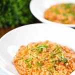 Tomato and mascarpone cheese risotto with basil chiffonade served in white bowls.