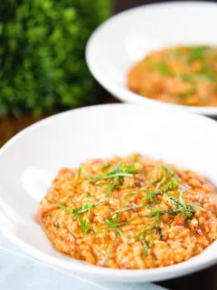 Tomato and mascarpone cheese risotto with basil chiffonade served in white bowls.