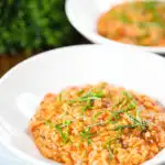 Tomato and mascarpone cheese risotto with basil chiffonade served in white bowls.