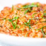 Close-up tomato and mascarpone cheese risotto with basil chiffonade served in a white bowl.