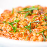 Close-up tomato and mascarpone cheese risotto with basil chiffonade served in a white bowl.