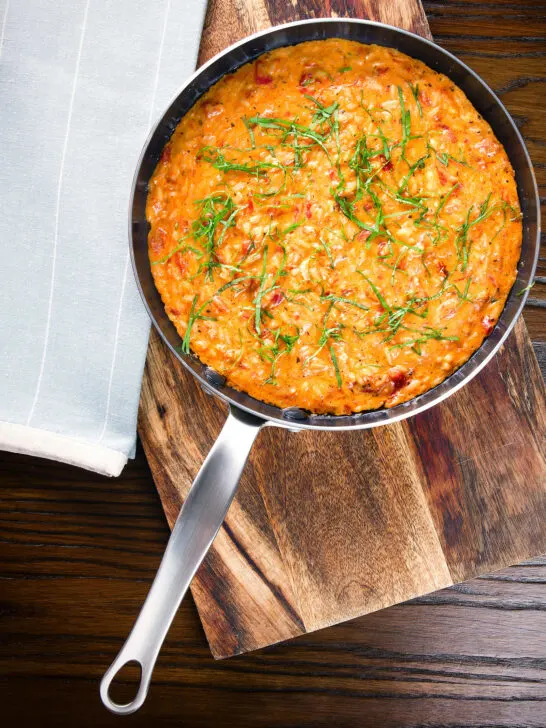 Overhead tomato and mascarpone cheese risotto with basil chiffonade served in a cooking pan.