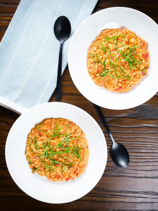 Overhead tomato and mascarpone cheese risotto with basil chiffonade served in white bowls.