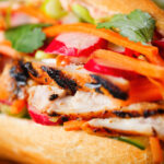 Close-up Vietnamese-influenced chicken banh mi sandwiches on a French baguette.