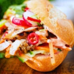 Close-up Vietnamese-influenced chicken banh mi sandwiches with quick pickles on a French baguette.