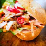 Close-up Vietnamese-influenced chicken banh mi sandwiches with quick pickles on a French baguette.