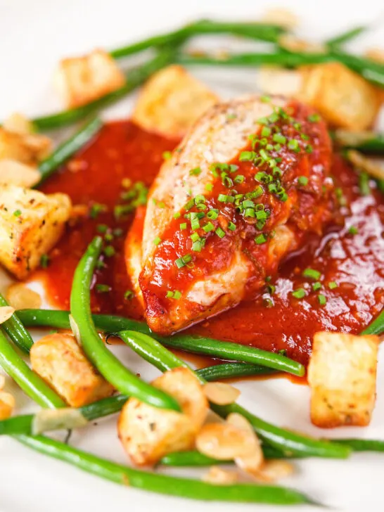 Chicken breast in tomato sauce served with Parmentier potatoes and green bean amandine.