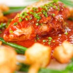 Close-up chicken breast in tomato sauce served with Parmentier potatoes and green bean amandine.
