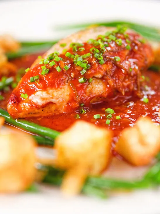 Close-up chicken breast in tomato sauce served with Parmentier potatoes and green bean amandine.