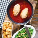 Overhead chicken in tomato sauce in a pan served with Parmentier potatoes and green bean amandine.