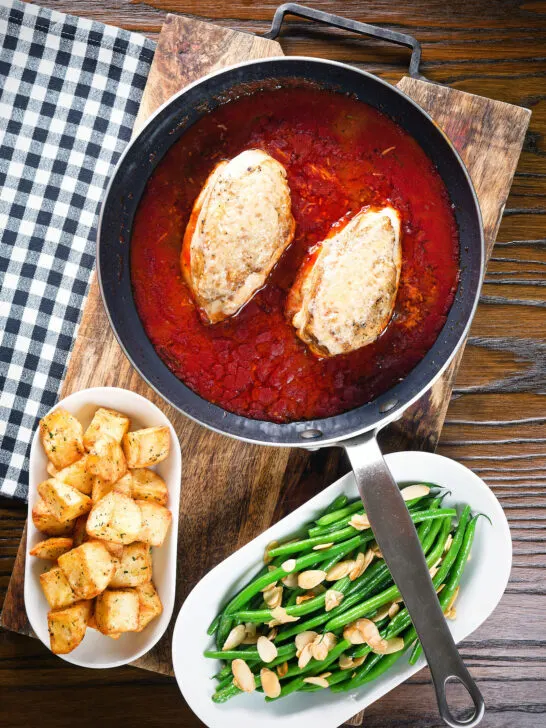 Overhead chicken in tomato sauce in a pan served with Parmentier potatoes and green bean amandine.
