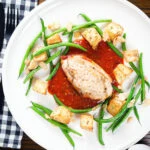 Overhead chicken breast in tomato sauce served with Parmentier potatoes and green bean amandine.