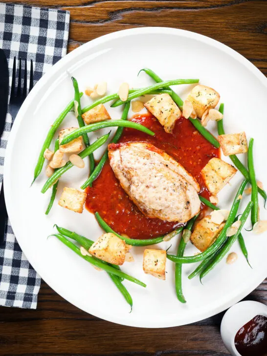 Overhead chicken breast in tomato sauce served with Parmentier potatoes and green bean amandine.