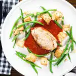 Overhead chicken breast in tomato sauce served with Parmentier potatoes and green bean amandine.