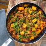 Overhead Cuban inspired minced beef picadillo with potatoes, raisins and capers in a cooking pan.