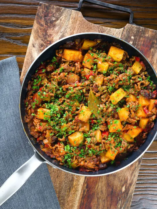 Overhead Cuban inspired minced beef picadillo with potatoes, raisins and capers in a cooking pan.