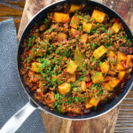 Overhead Cuban inspired minced beef picadillo with potatoes, raisins and capers in a cooking pan.