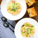 Overhead creamy gnocchi carbonara with pecorino cheese and fresh parsley served with garlic bread.