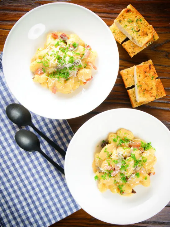 Overhead creamy gnocchi carbonara with pecorino cheese and fresh parsley served with garlic bread.