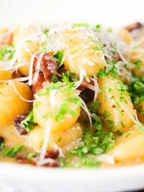 Close-up creamy gnocchi carbonara with pecorino cheese and fresh parsley.