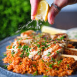 Lemon wedge being squeezed over Greek chicken souvlaki skewers.