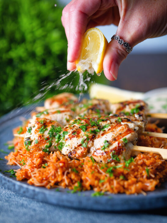 Lemon wedge being squeezed over Greek chicken souvlaki skewers.