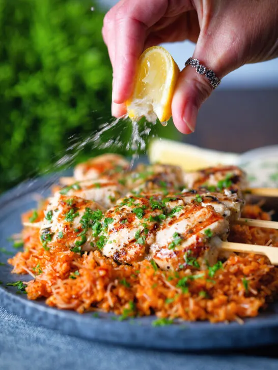 Lemon wedge being squeezed over Greek chicken souvlaki skewers.
