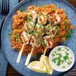 Overhead Greek chicken souvlaki kebabs served with pourgouri and a yoghurt sauce.