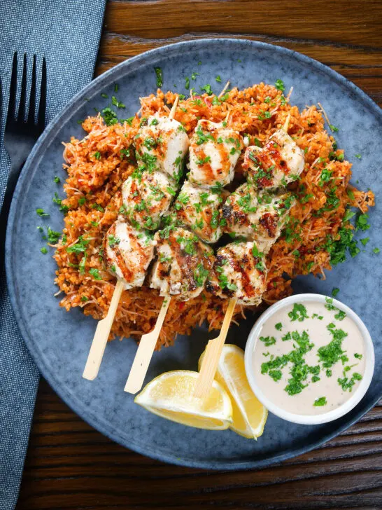 Overhead Greek chicken souvlaki kebabs served with pourgouri and a yoghurt sauce.