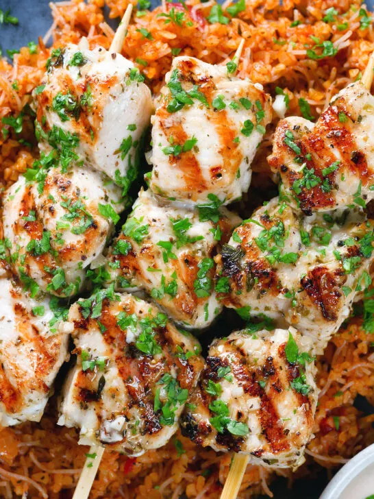 Close-up overhead Greek chicken souvlaki kebabs served with pourgouri and a yoghurt sauce.