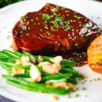 Pork chops in BBQ sauce served with green beans amandine and hasselback potato.