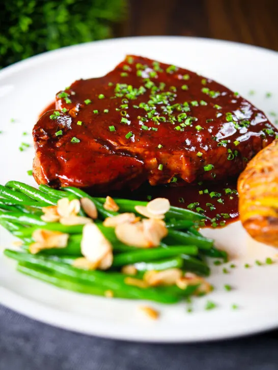 Pork chops in BBQ sauce served with green beans amandine and hasselback potato.