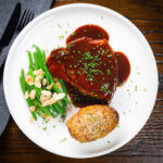 Oven baked pork chops in BBQ sauce served with green beans amandine and hasselback potato.