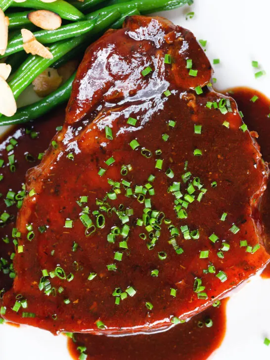 Overhead close up pork chops in BBQ sauce served with green beans amandine.