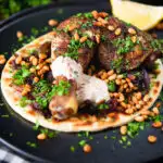 Sumac chicken musakhan with caramelised onions, pine nuts and yoghurt served on flatbread.