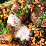 Close-up sumac chicken musakhan with caramelised onions, pine nuts and yoghurt served on flatbread.