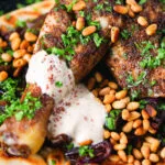 Close-up sumac chicken musakhan with caramelised onions, pine nuts and yoghurt served on flatbread.
