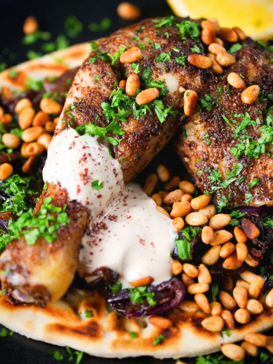 Close-up sumac chicken musakhan with caramelised onions, pine nuts and yoghurt served on flatbread.