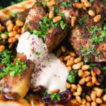 Close-up sumac chicken musakhan with caramelised onions, pine nuts and yoghurt served on flatbread.