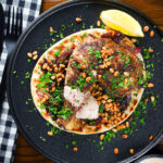 Overhead sumac chicken musakhan with caramelised onions, pine nuts and yoghurt served on flatbread.