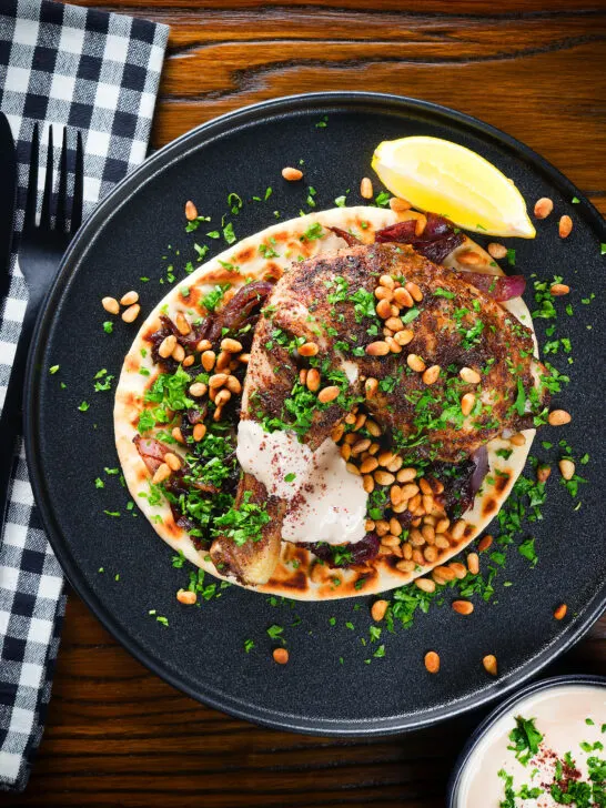 Overhead sumac chicken musakhan with caramelised onions, pine nuts and yoghurt served on flatbread.